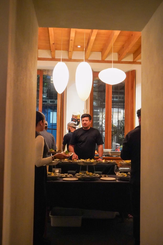 Chef Tomás Bermudez de La Docena en el Evento Petit del Festival Climats. Esta en una cocina abierta estilo mexicana, con platos de ostiones y tostadas.